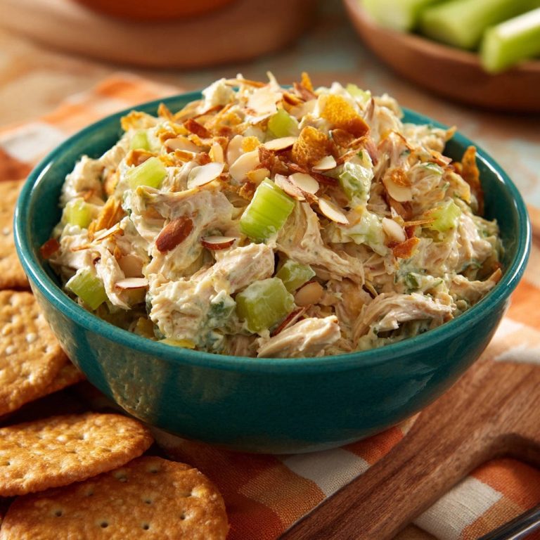 Cremiger Hähnchensalat in einer türkisfarbenen Schüssel serviert, garniert mit Mandelsplittern und Selleriestückchen. Ein köstliches Mittagessen.