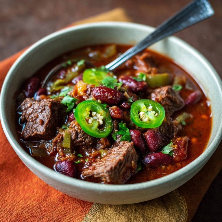 Herzhaftes Rindfleisch Chili in einer Schüssel serviert, garniert mit Jalapeño-Scheiben und frischer Petersilie. Der Blick aus der Nähe offenbart die zarte Fleischtextur.