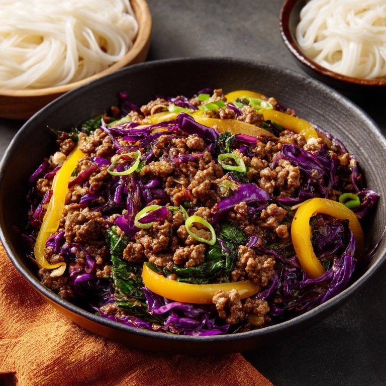 Asiatische Hackfleischpfanne mit Rotkohl & Paprika in einer Schüssel von oben, serviert mit Reisnudeln, garniert mit frischen Frühlingszwiebeln.