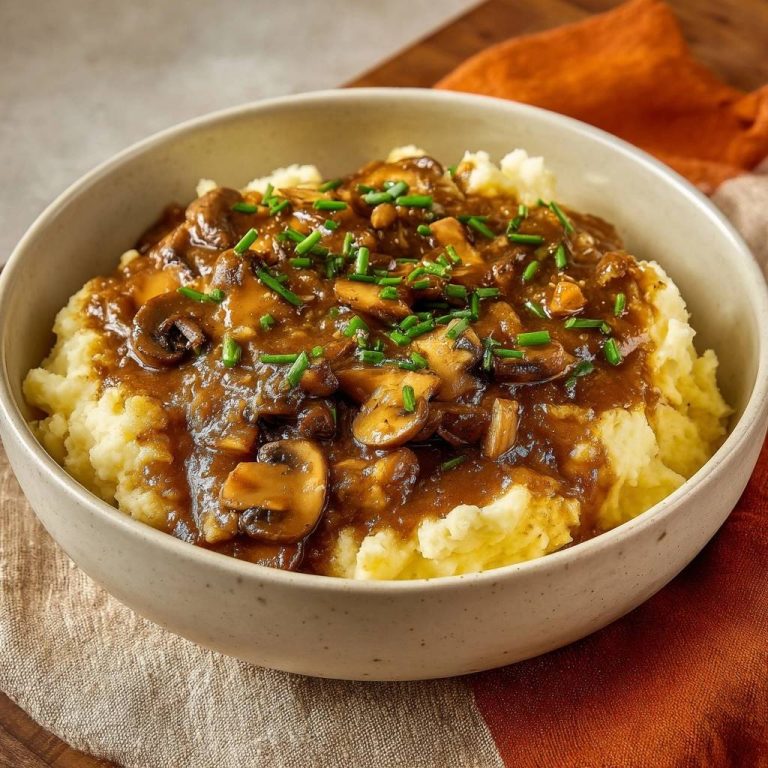Cremiges Kartoffelpüree mit Pilzsoße, serviert in einer cremefarbenen Schüssel, garniert mit frischen Kräutern. Ein herzhaftes Gericht, perfekt für kalte Tage.