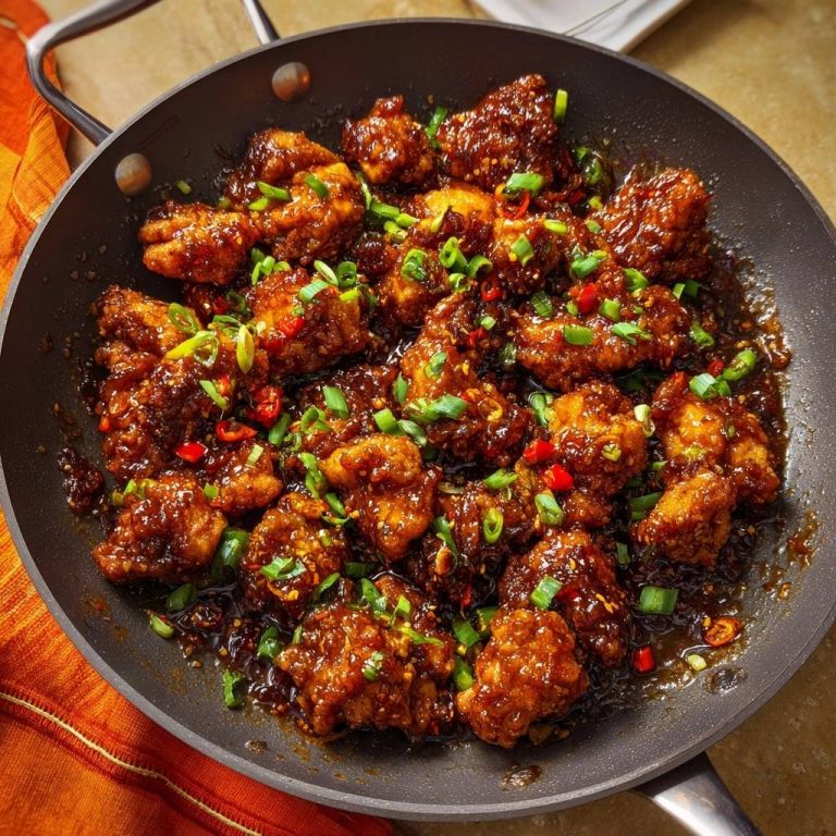 Knuspriges Chili-Hähnchen in einer Pfanne, garniert mit frischen Kräutern und Chilis, aus der Vogelperspektive fotografiert.