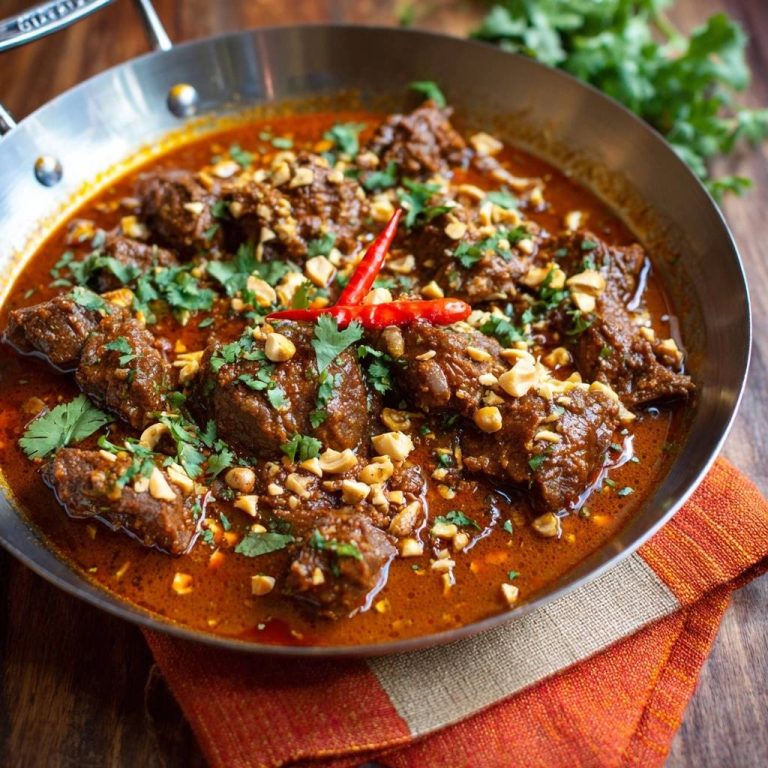 Saftiges Rindfleisch-Erdnuss-Curry serviert in einer Pfanne, garniert mit Erdnüssen und frischem Koriander. Ein köstliches Curry Gericht.