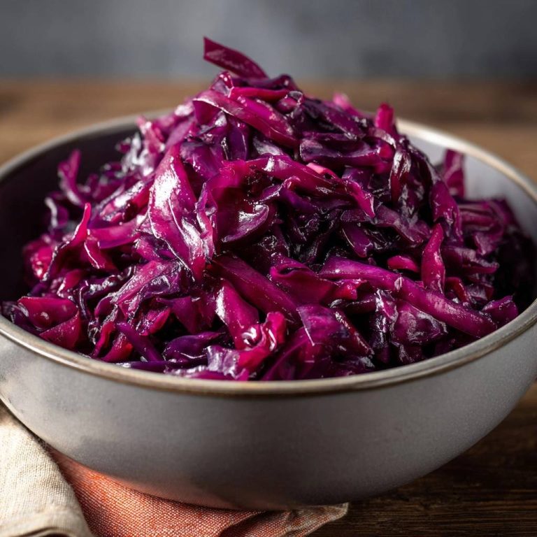 Bissfester Rotkohl in einer dunklen Schüssel von oben gesehen, mit glänzenden, violetten Kohlblättern und einer rustikalen Holzoberfläche.