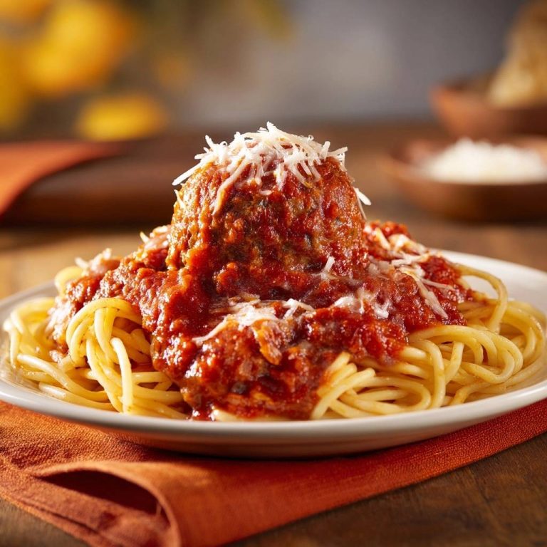 Spaghetti mit saftigen Fleischbällchen, serviert auf einem weißen Teller, garniert mit geriebenem Käse und serviert auf einem orangefarbenen Untersetzer.