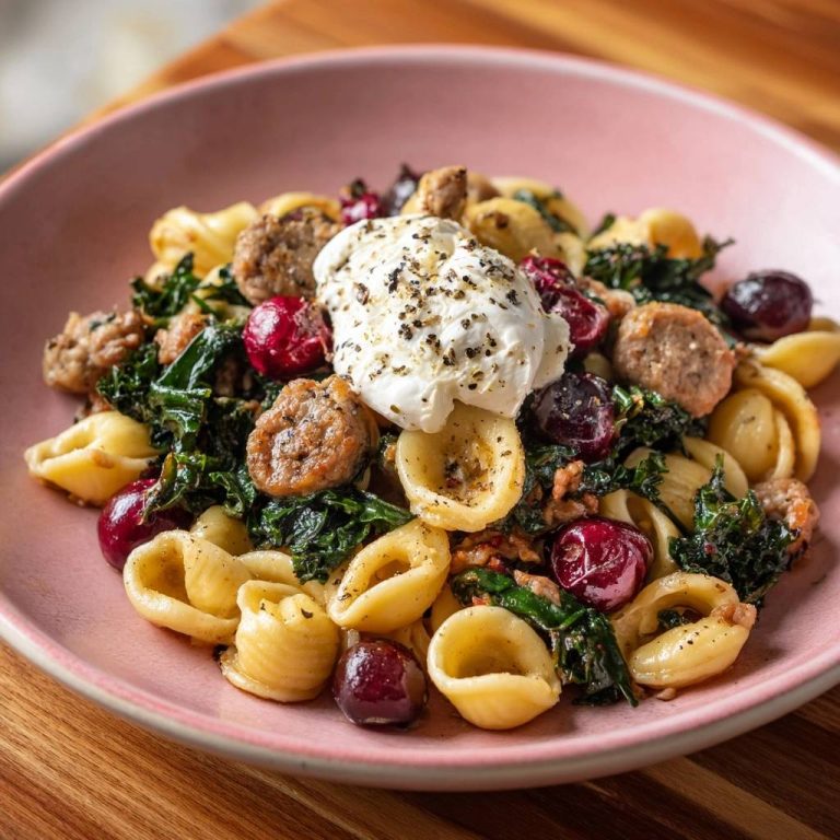 Orecchiette mit Wurst, Grünkohl, Kirschen und Burrata in einer Schüssel, serviert aus der Vogelperspektive mit einem Klecks Burrata.