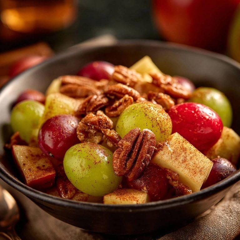 Herbstlicher Obstsalat mit Pekannüssen und Zimt, serviert in einer dunklen Schüssel, zeigt eine Nahaufnahme der fruchtigen und nussigen Zutaten.