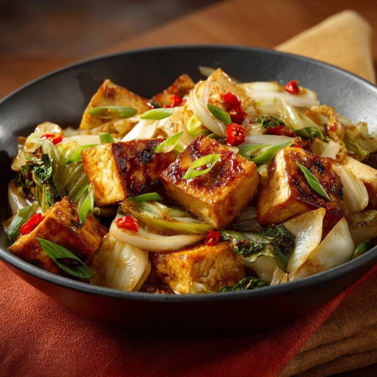 Knuspriger Tofu-Wok mit Lauch, Chili & Pak Choi in einer Nahaufnahme, serviert in einer schwarzen Schüssel mit frischen Frühlingszwiebeln.