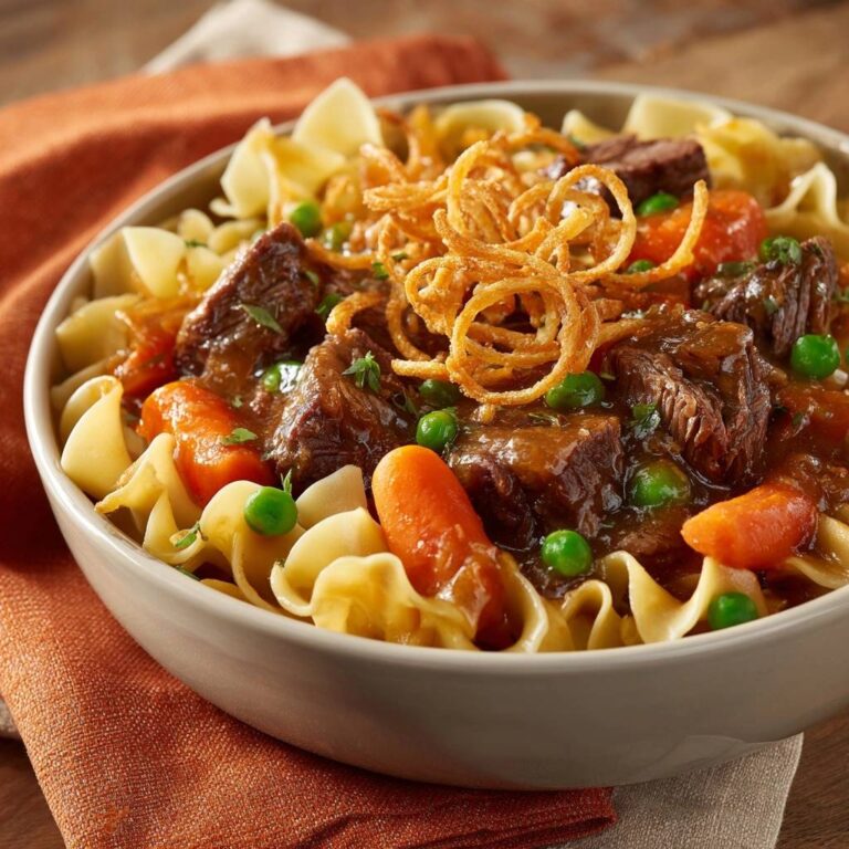Herzhaftes Rindergulasch mit Eiernudeln serviert in einer Schüssel, garniert mit knusprigen Zwiebeln und Erbsen. Ein herzhaftes Gericht zum Genießen.